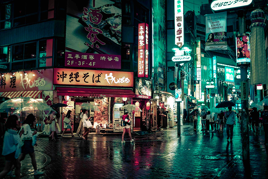 People walk down the street in Tokyo, Japan, at night with colorful street signs lit up.