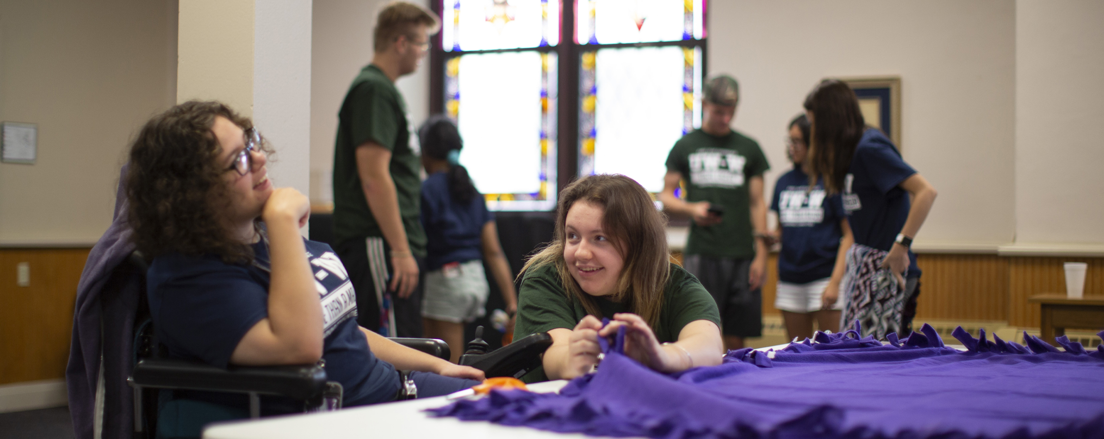 Two students help make blankets at a church.