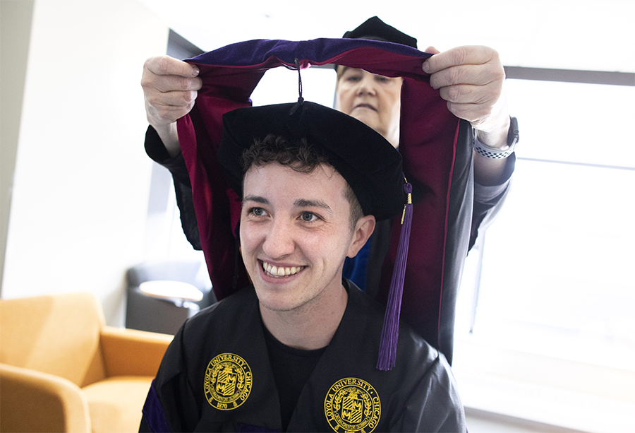 A faculty member places an academic hood on a smiling student.
