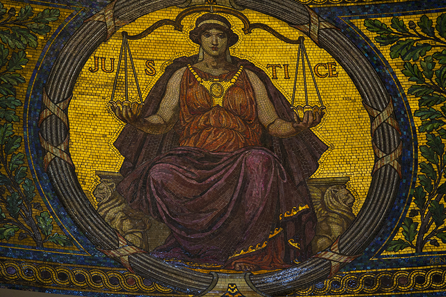 A mosaic of yellows, greens and blues shows a person in a flowy dress holding scales of justice.