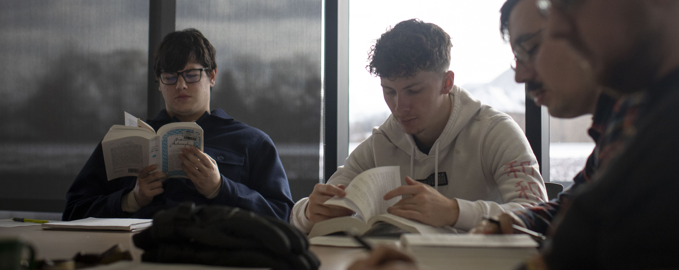 Students gather around a table reading books.