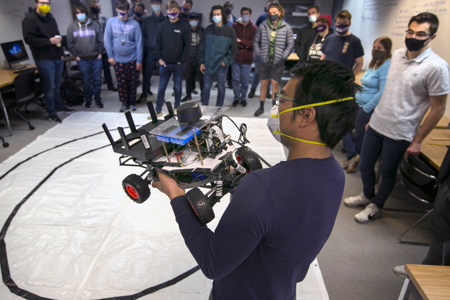 Students stand around a professor who is holding a self driving car.