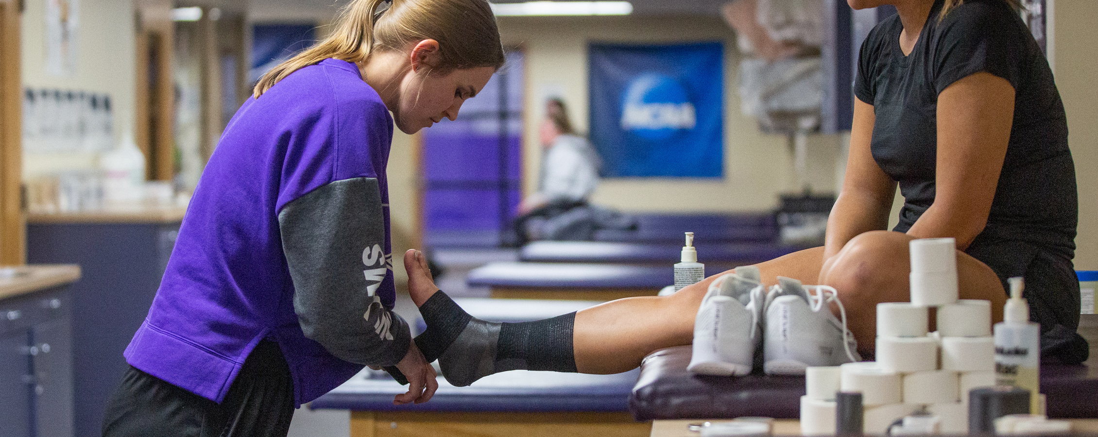 A student wraps the ankle of an athlete.