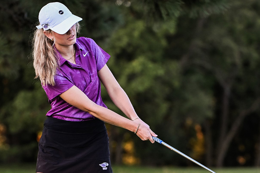 A person in a white hat and purple shirt swings a golf club.