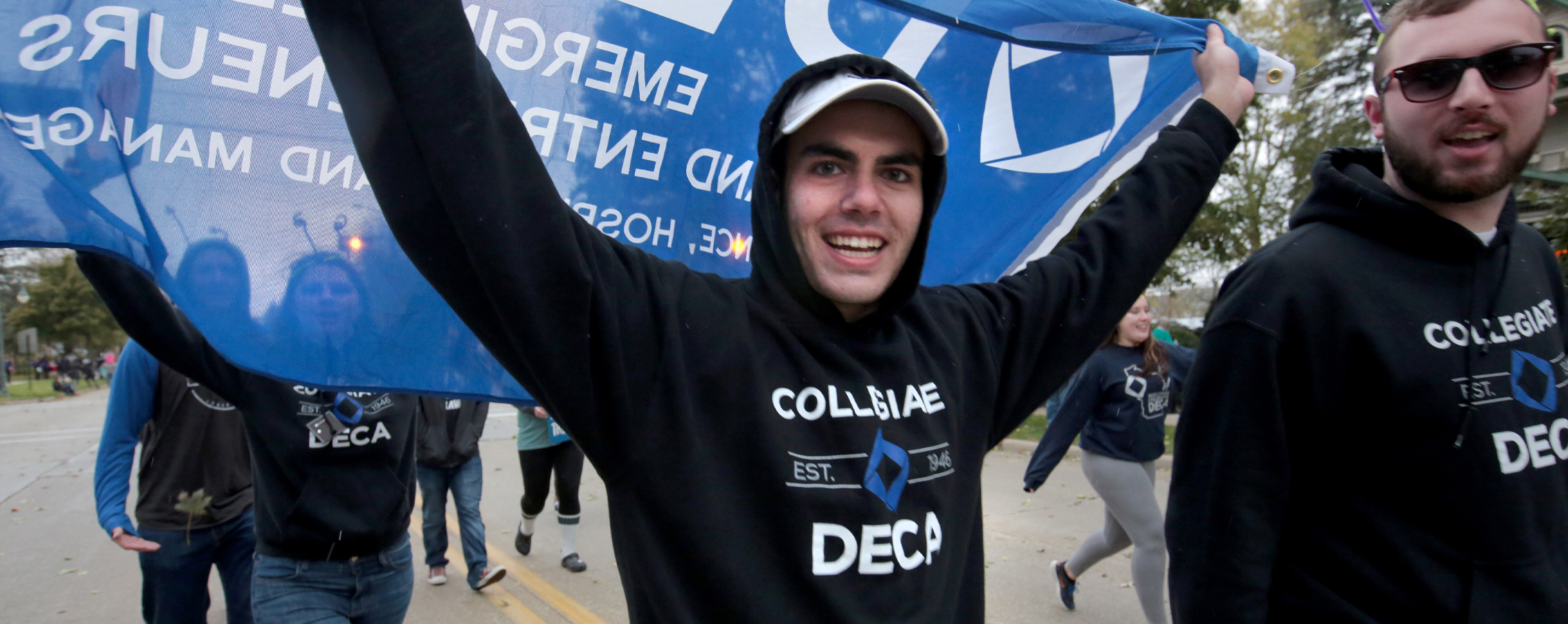 A student wears a DECA shirt and waves a DECA flag.