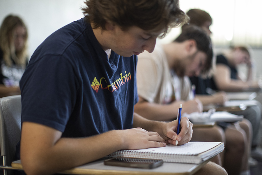 A student sits at a desk writing in a notebook.