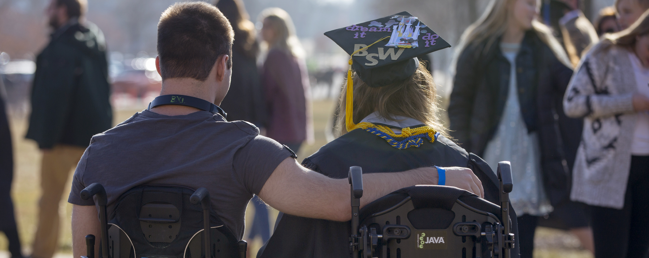 Two people in wheelchairs with their arms around each other at graduation.