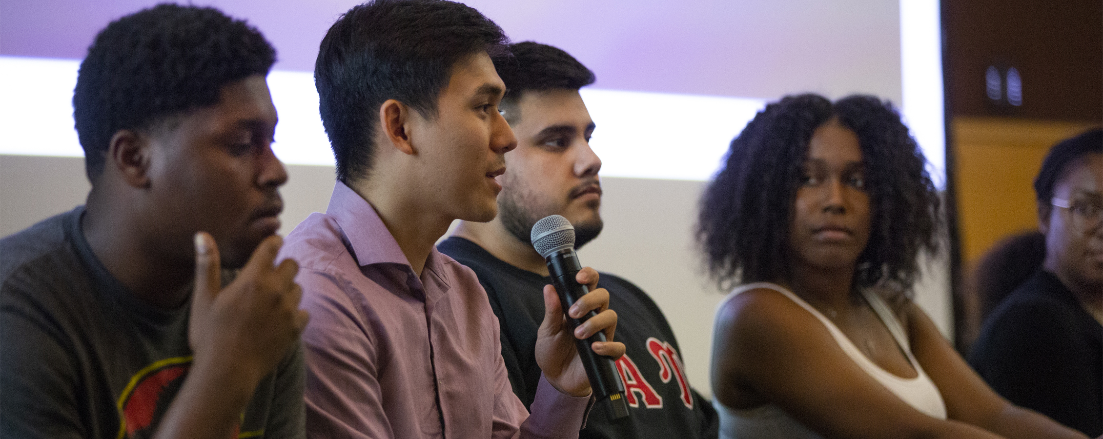 Four students are seated in the front of a room speaking into a microphone.