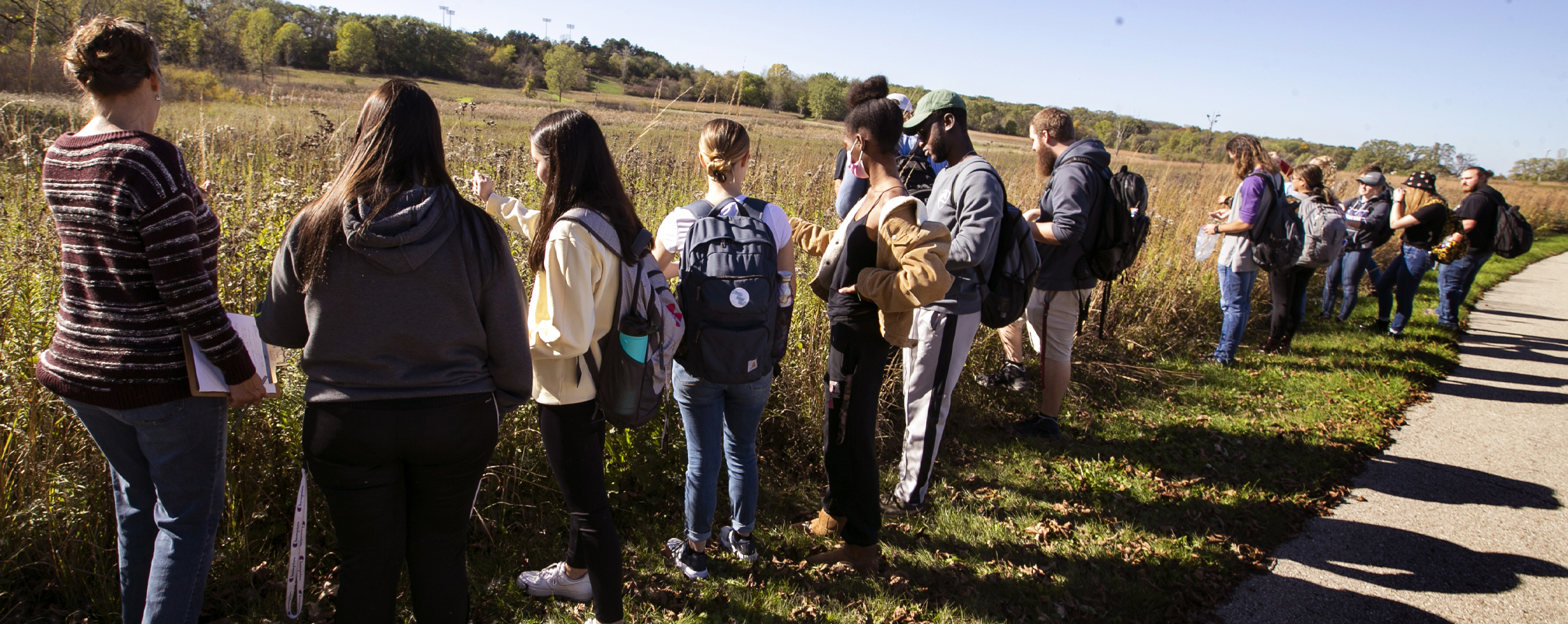 A sociology class stands by a prairie, outdoors.