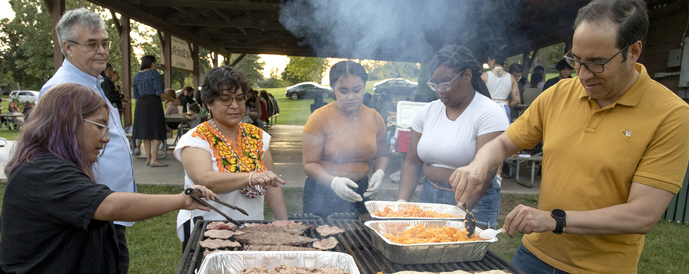 People gather around outdoor grills making food.