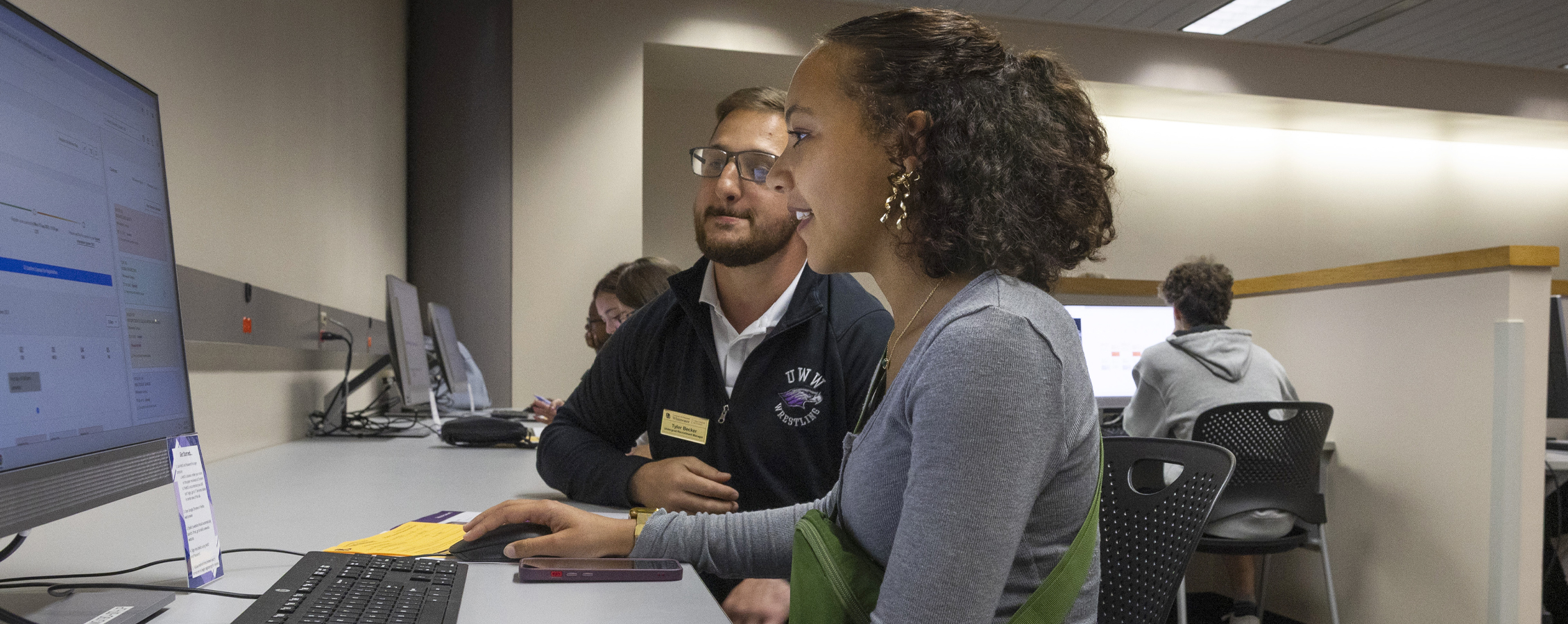 A student sits in front of a computer with an advisor sitting next to them.