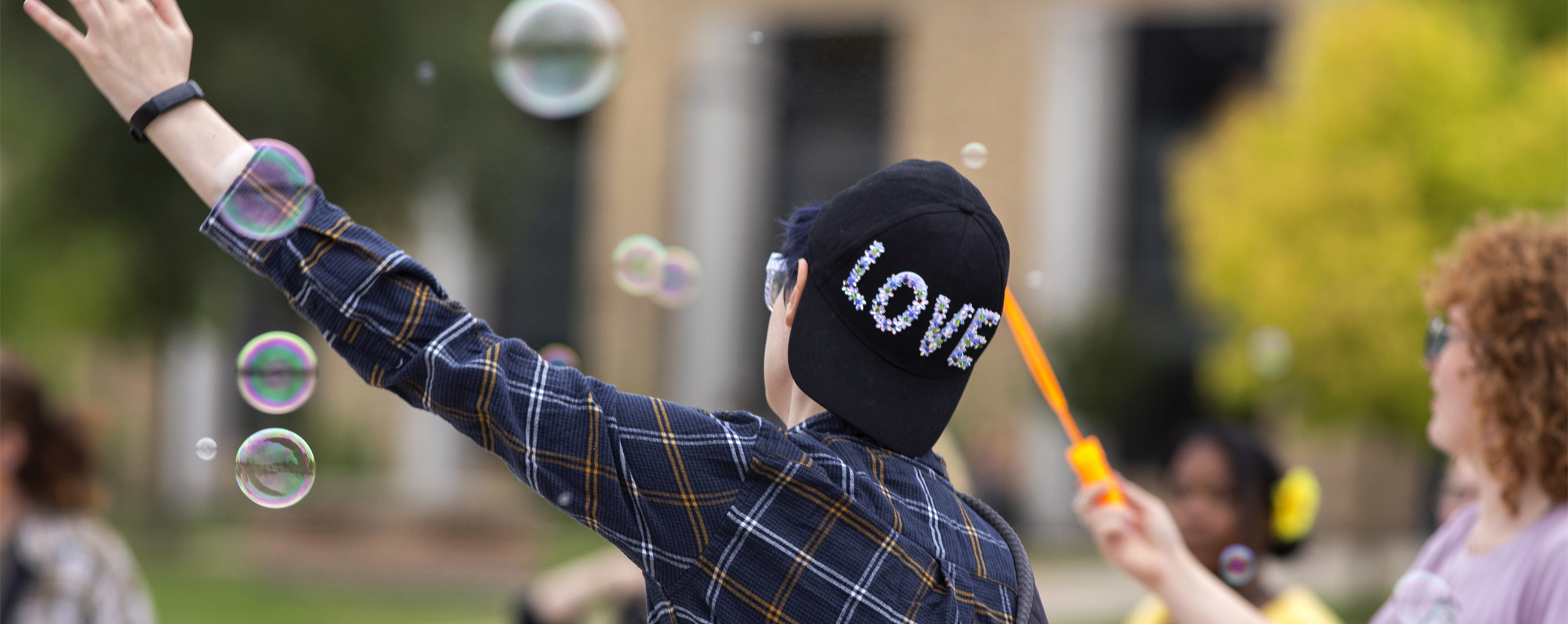 A person wears a hat that says love while bubbles float in the air.