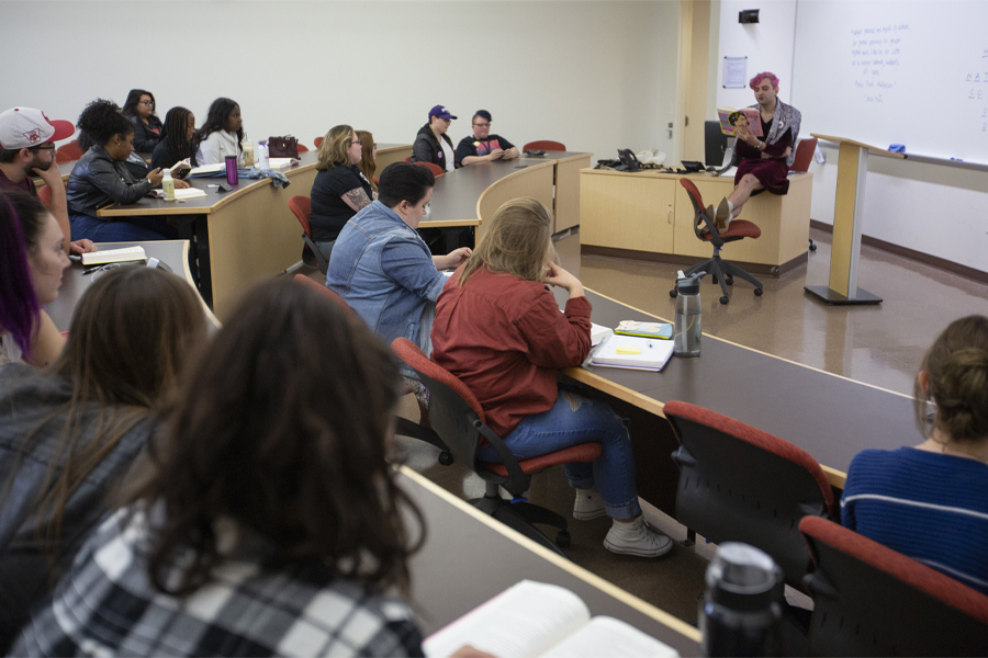 A person with pink hair reads at the front of class.