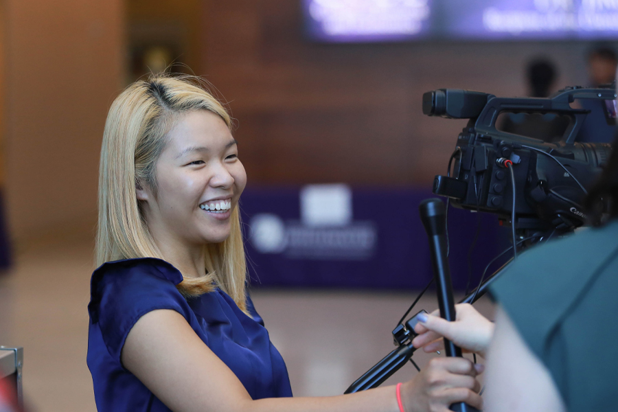 A student smiles while using a video camera.