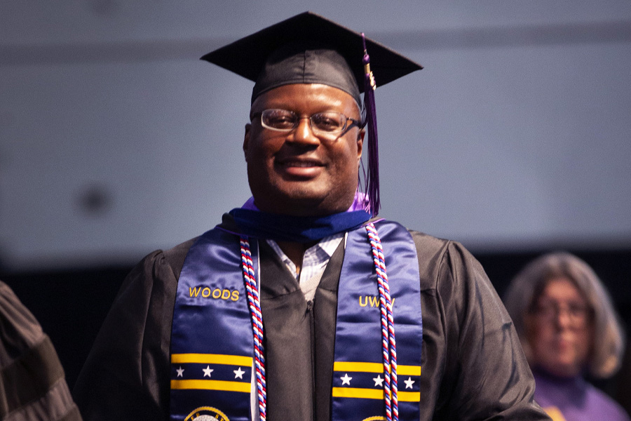 A graduate wearing a Master's hood smiles as they cross the stage at Commencement.