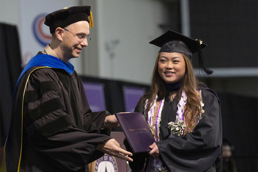 A Master's graduate is handed their diploma as they cross the stage at Commencement. 