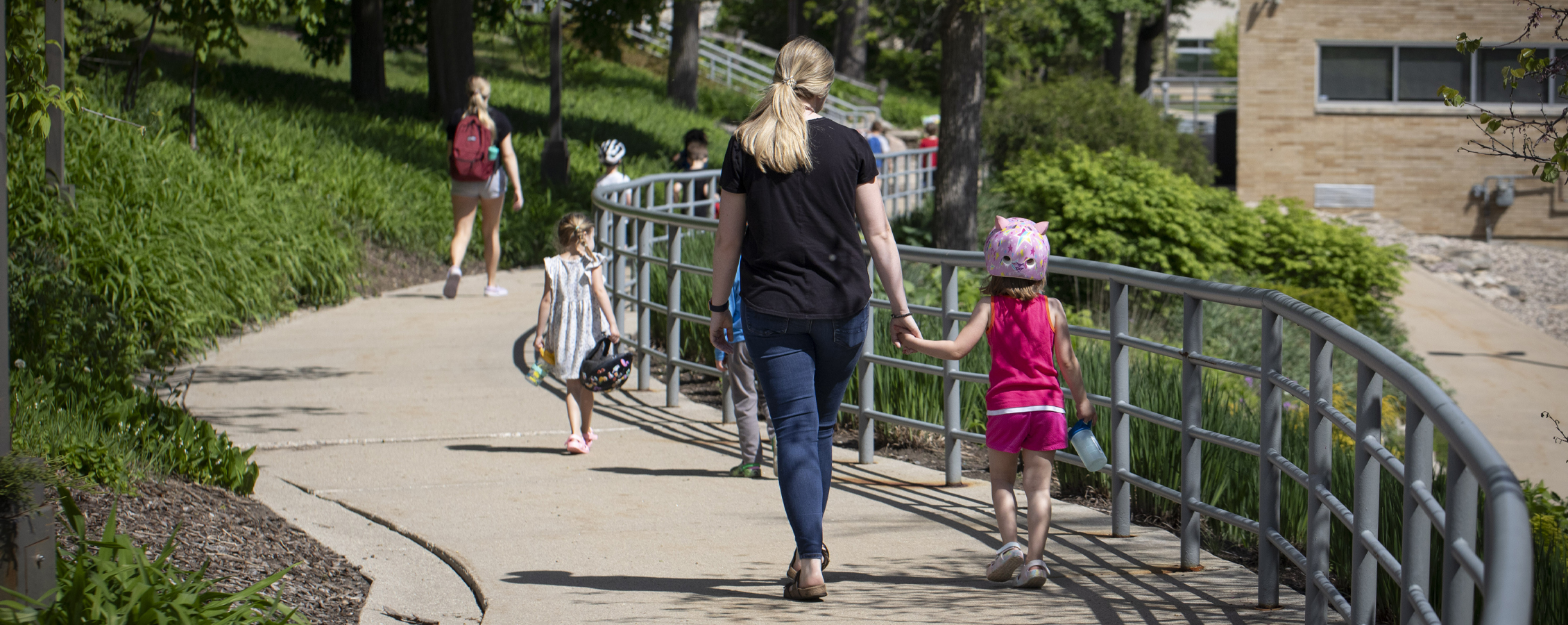 A student holds hands with a child as they walk down a sidewalk on the UW-Whitewater campus.