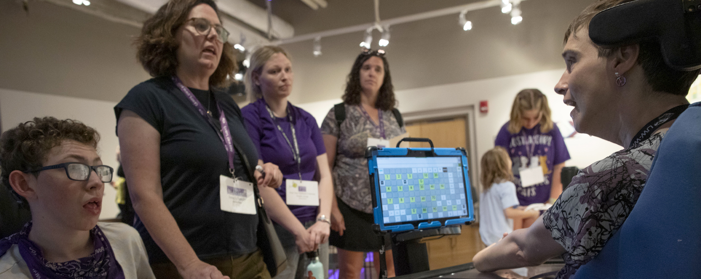 People gather in Roberta's Art Gallery and converse with a person who uses a device for communication.