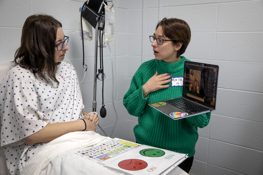A simulation is performed where a person sits in a hospital bed with a green-yes and a red-no board in front of them while another person looks on and asks questions.