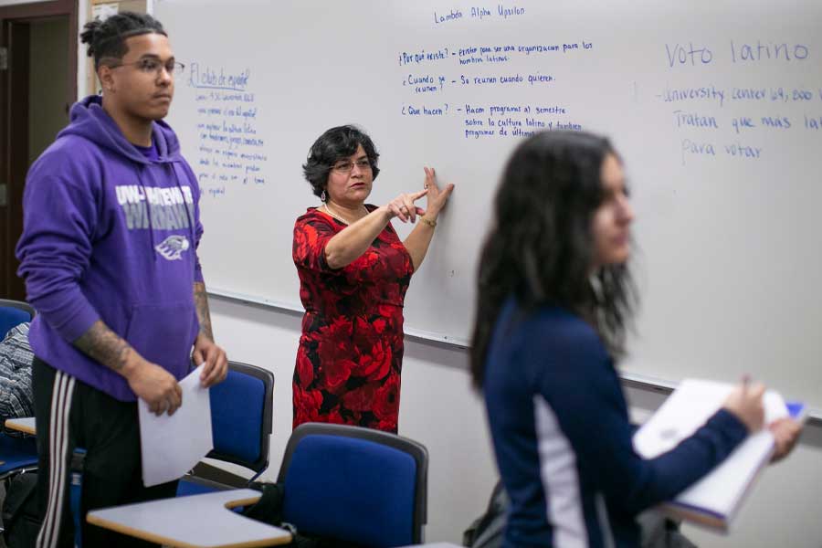 un profesor y dos estudiantes en una pizarra con español escrito en ella.