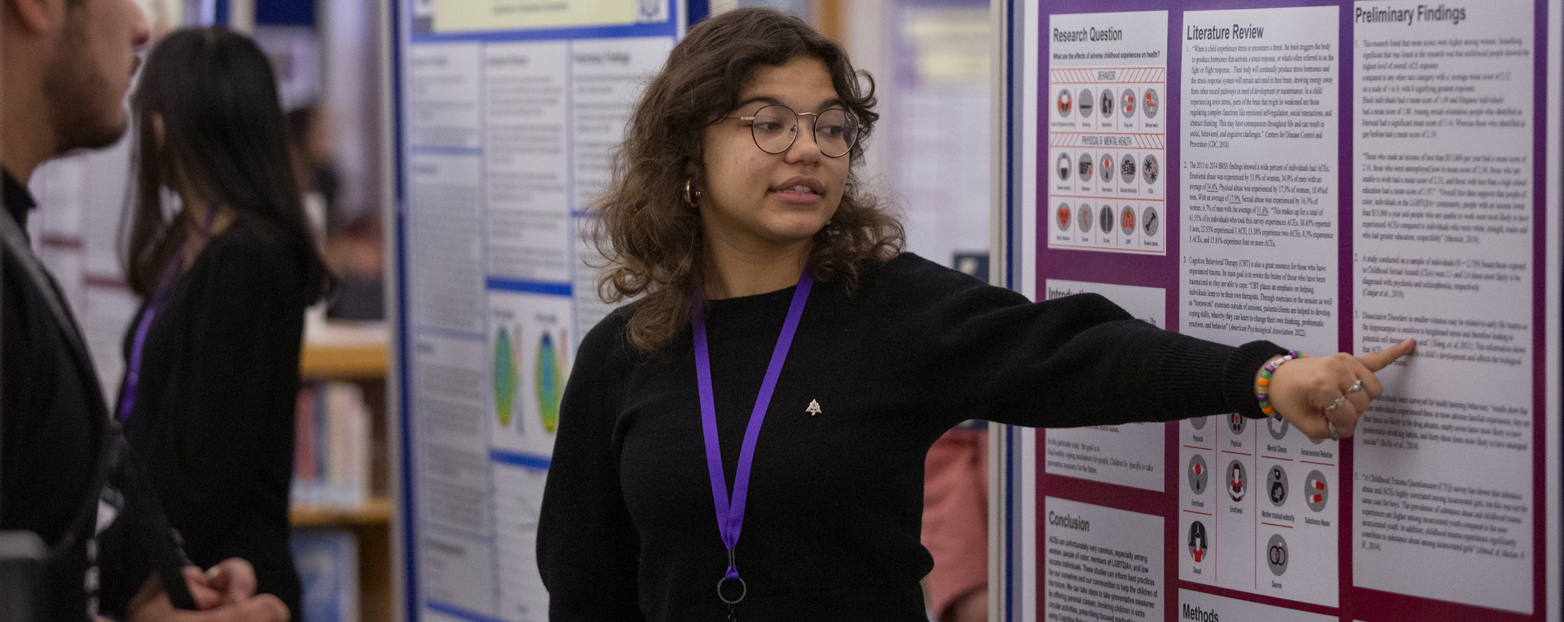 A student speaks while pointing to their research poster.
