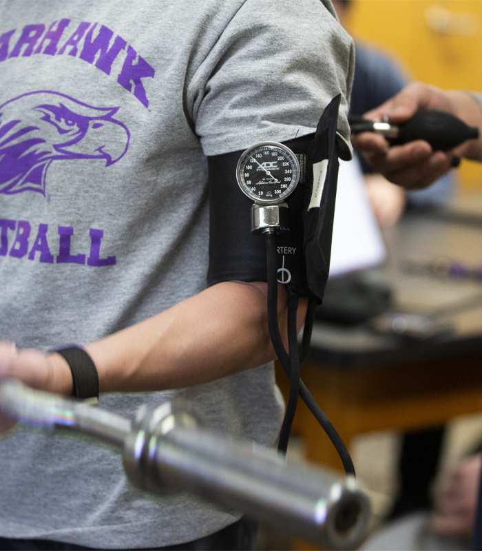 A student lifts a barbell with a monitor cuff on their bicep.