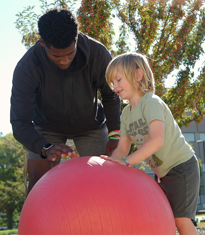 A student bounces a large red ball with a child.