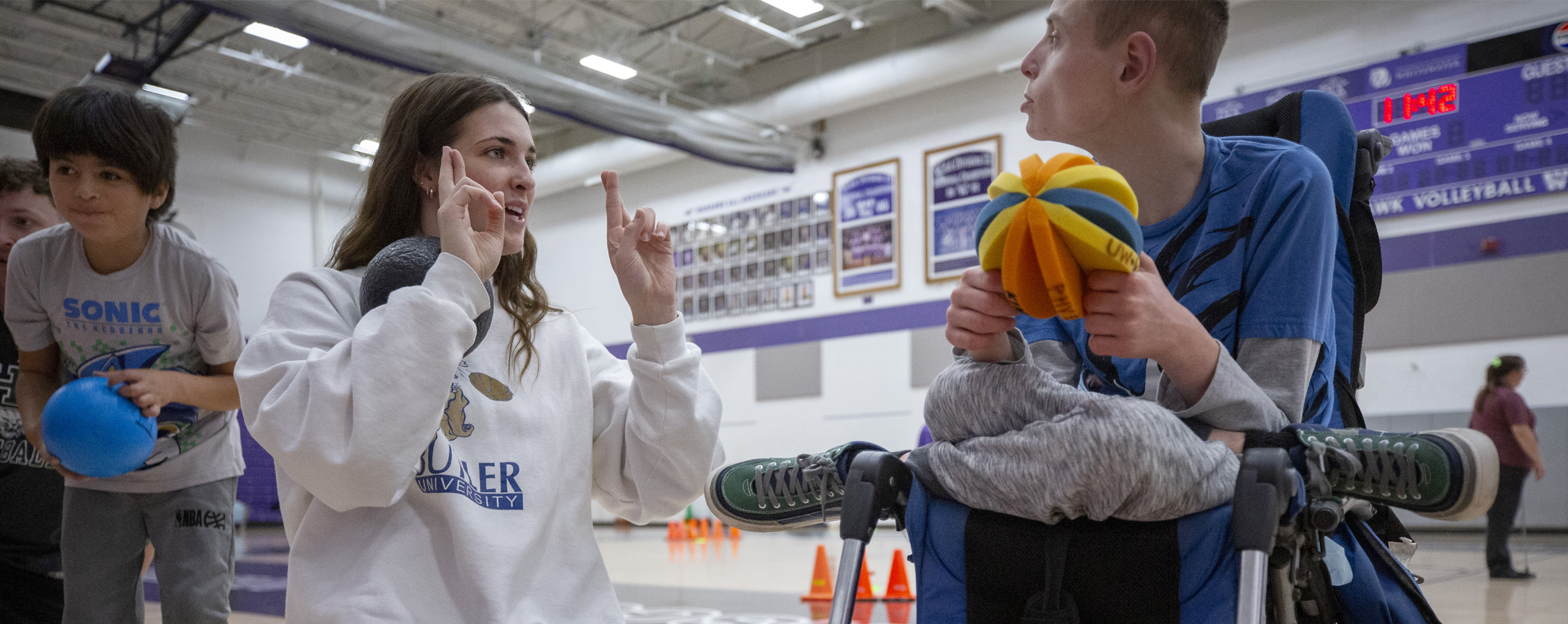 Woman using sign language to communicate with young boy holding toy ball.