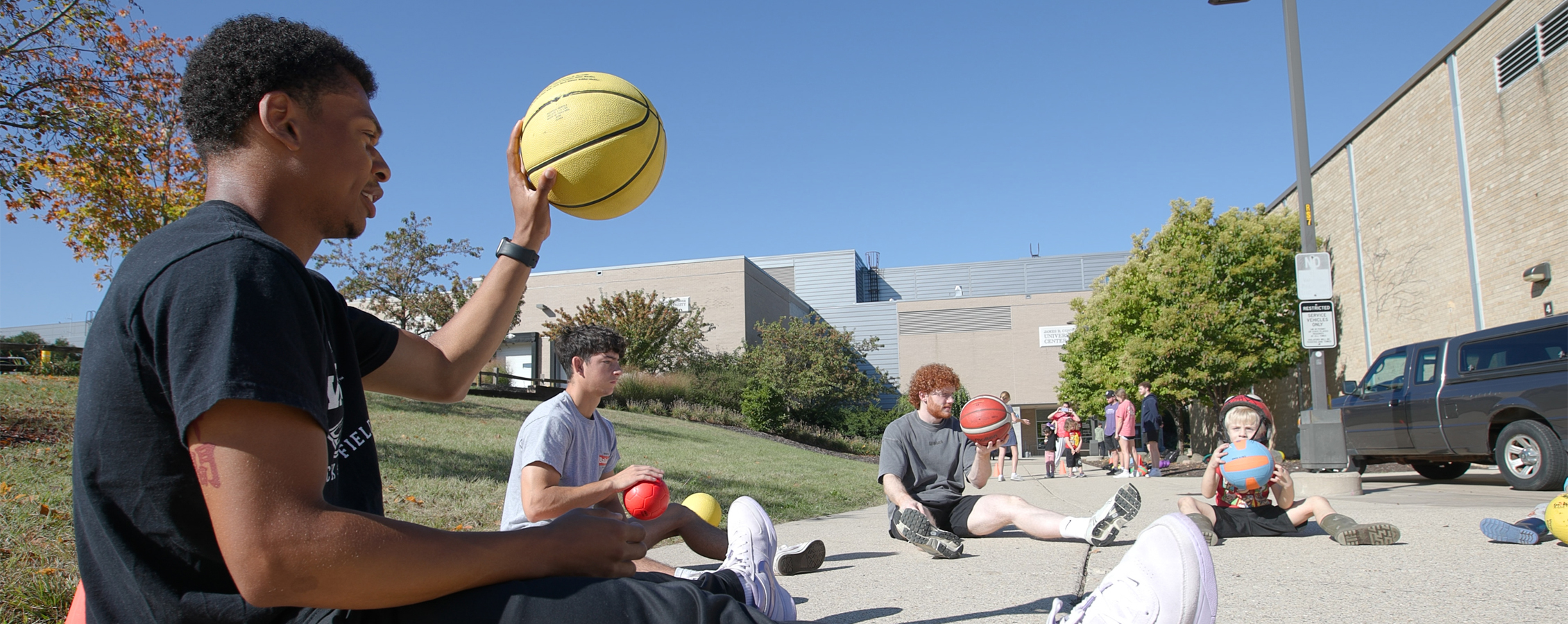 PE students sit in a circle with children as they show how to palm a basketball.