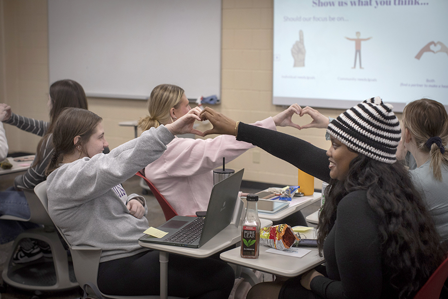 Students sit across form each other and connect their hands to make a heart.