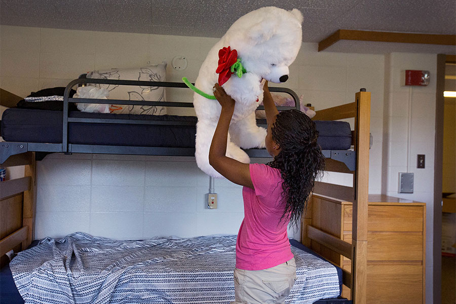 Student lifts large teddy bear in dorm room.