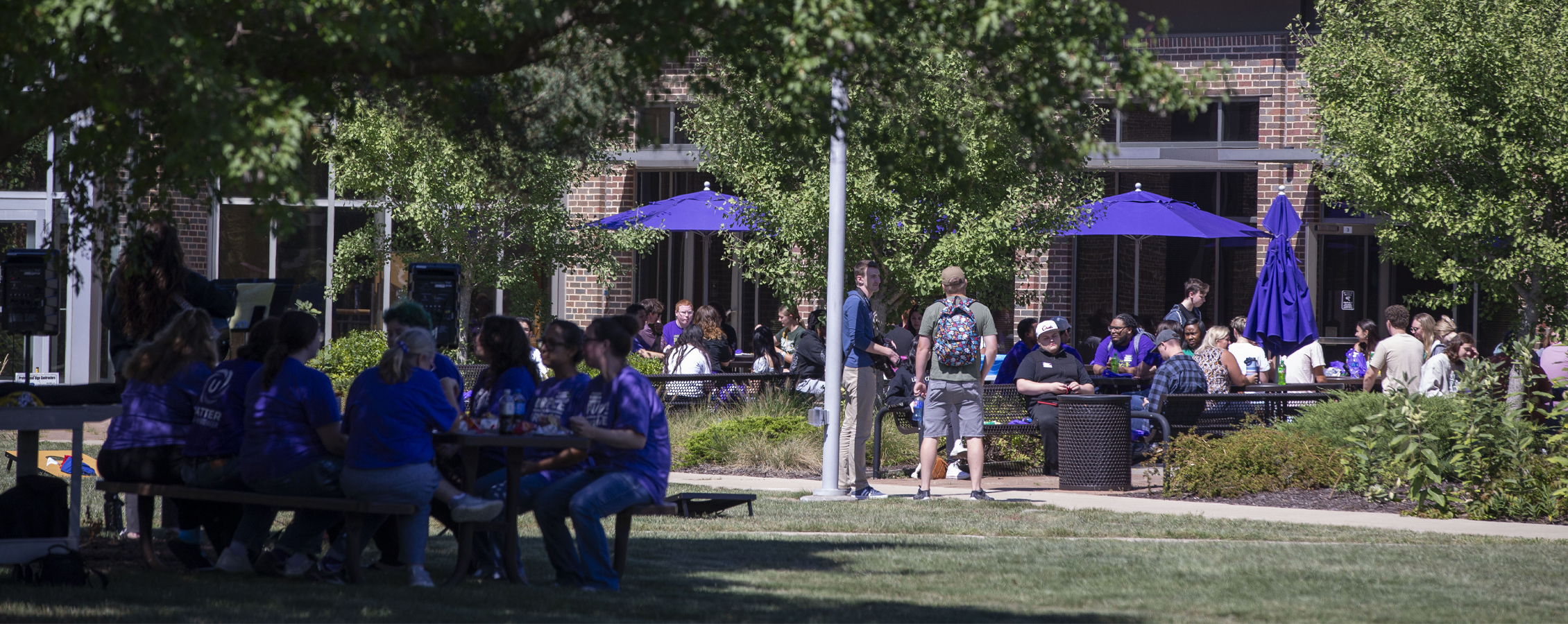 People sit at outdoor tables surrounded by trees on the URock campus.