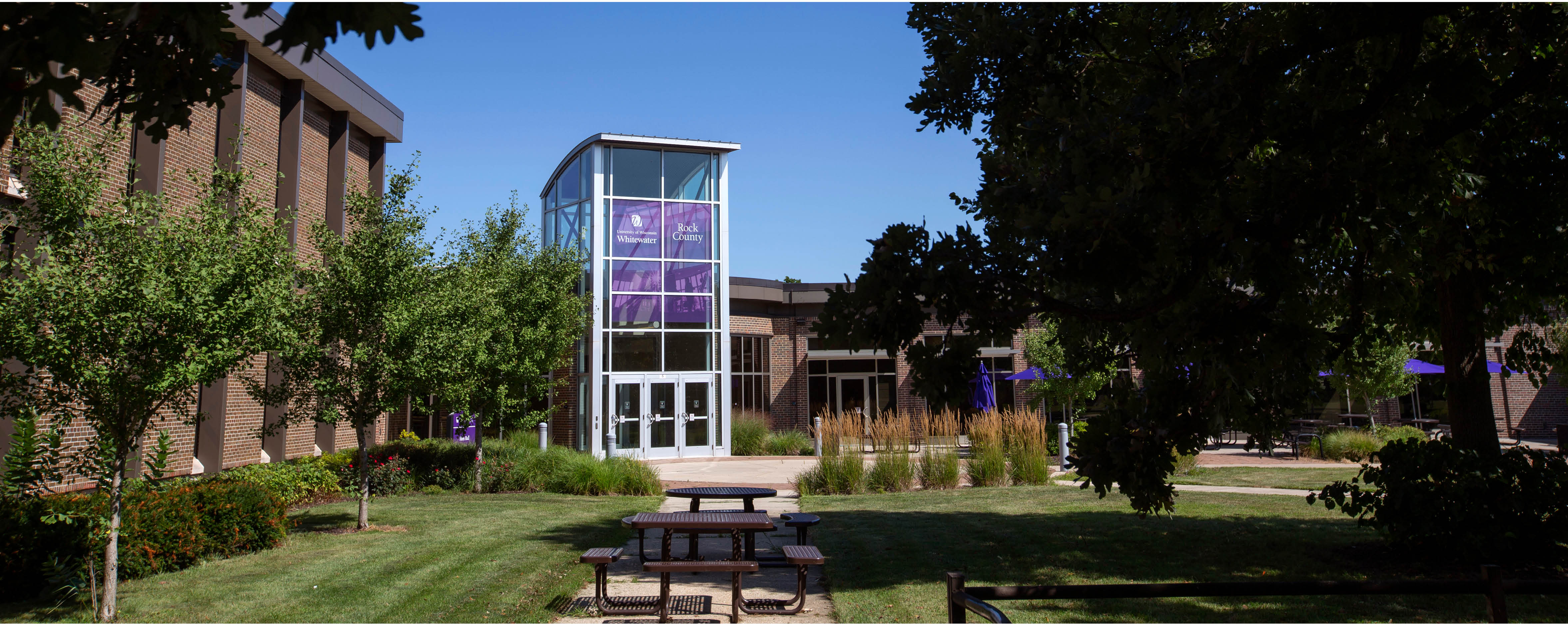 A courtyard leads to Rock County's main building with a purple banner on the windows that says UW-Whitewater Rock County.