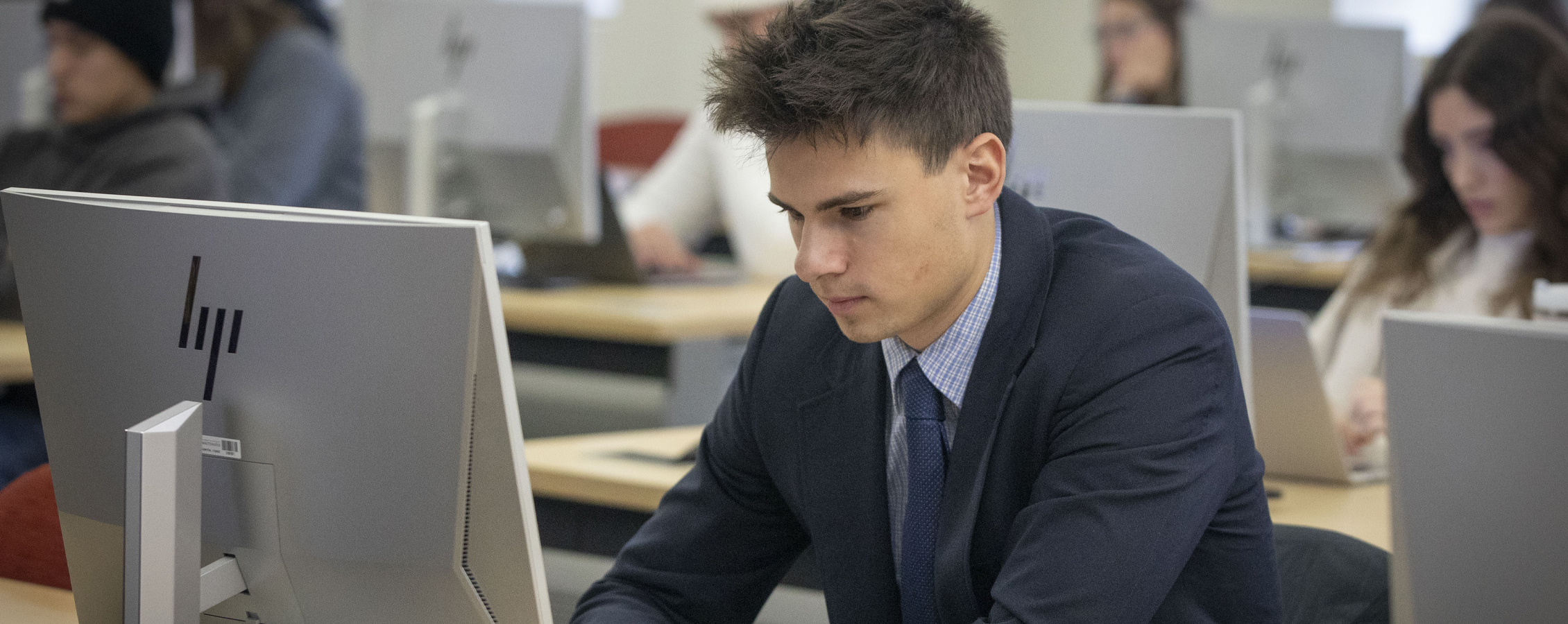 A student in a blue blazer works on a computer in a classroom.