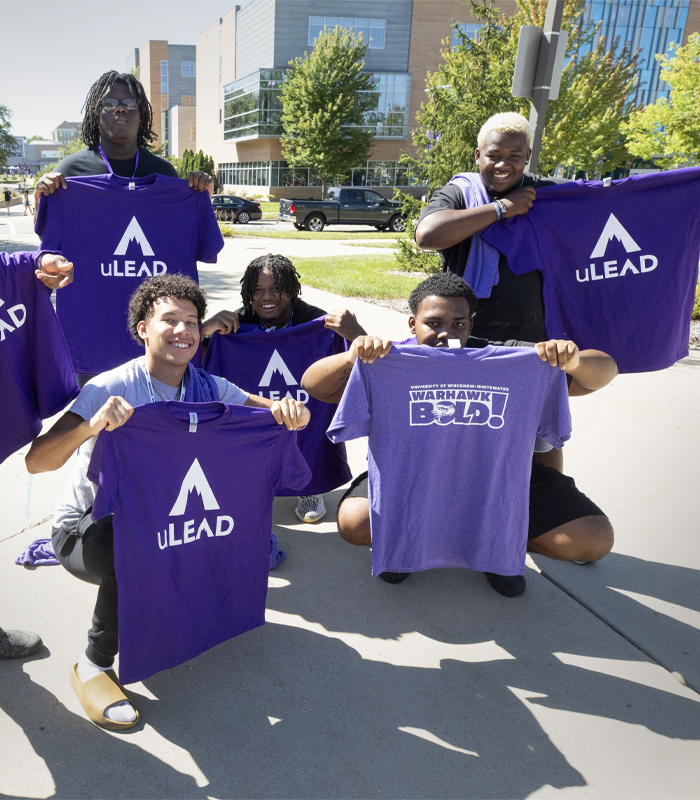 A group of students hold up purple shirts that say ULead.