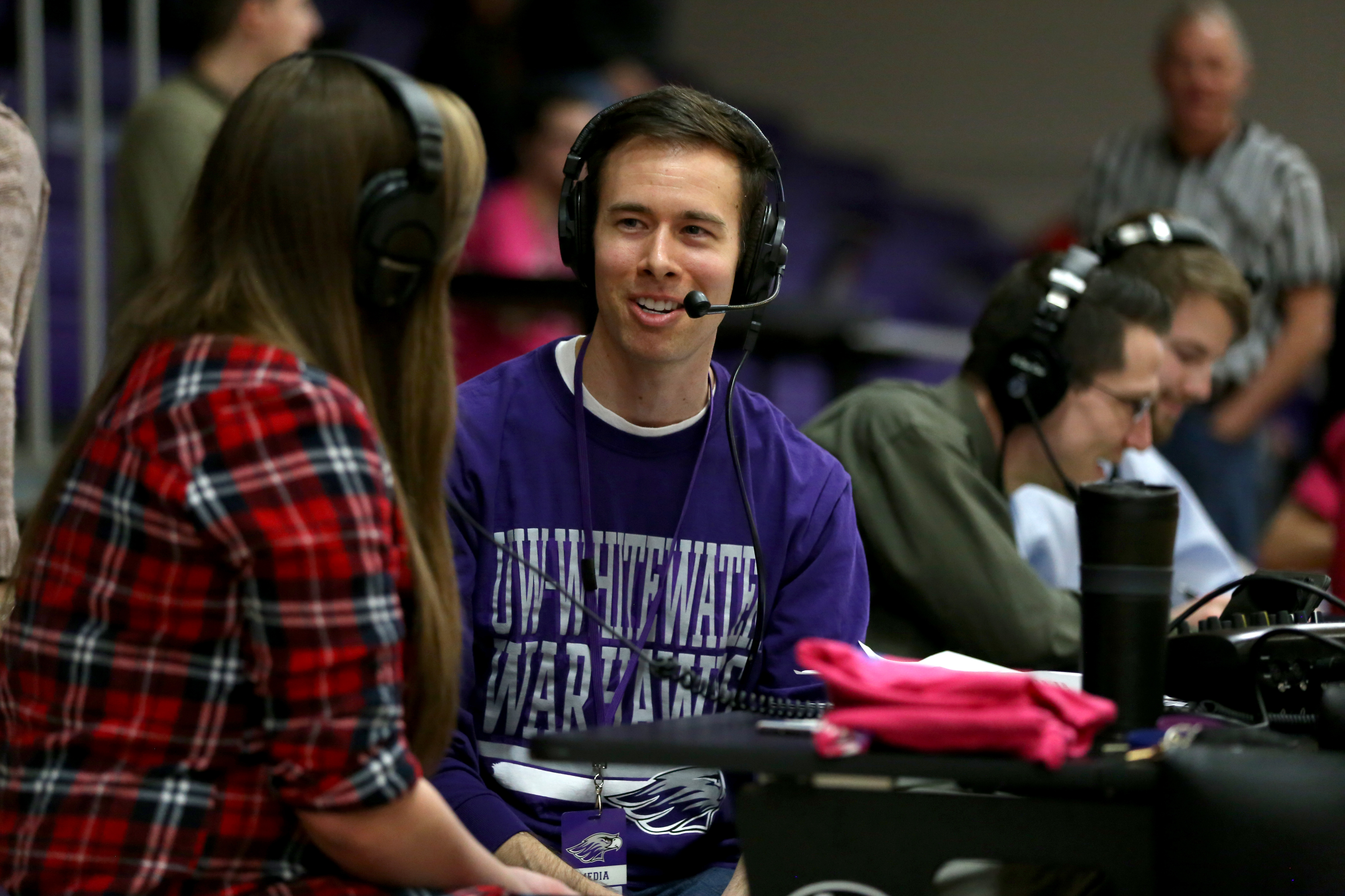 Jeff Angileri, wearing a purple UW-Whitewater shirt and headset, interviews a person in a plaid shirt.