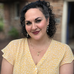 Maria Glorioso stands in front of a brick wall wearing a yellow shirt.