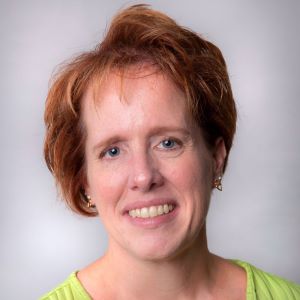 Becky Mueller stands in front of a white wall wearing a lime green shirt.