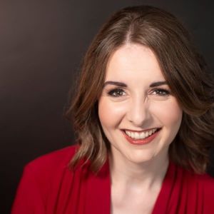 Dr. Rachel Wood smiles while wearing a red shirt sitting in front of a dark background.