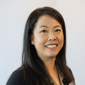 Headshot of May Vang wearing a black sweater standing in front of a white wall.