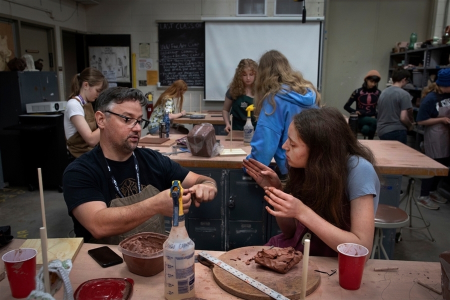 Instructor show student how to mold clay