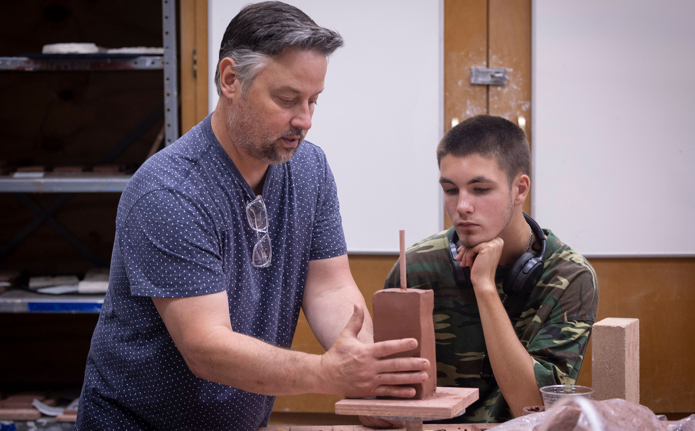 Ceramics teacher showing a student how to structure and cut a brick of clay
