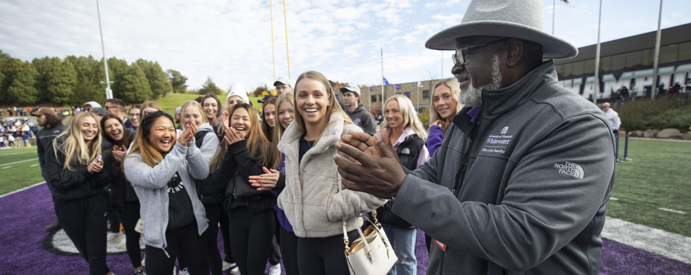 Chancellor King claps while standing on the football field.