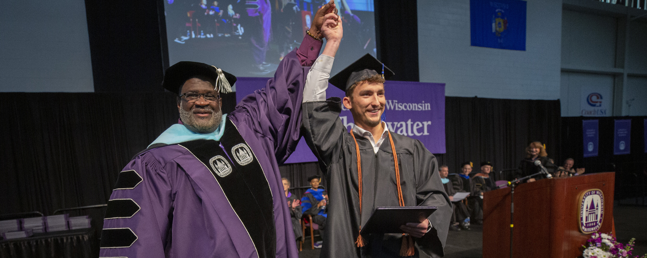 Chancellor King holds up the hand of a graduate as they cross the stage.