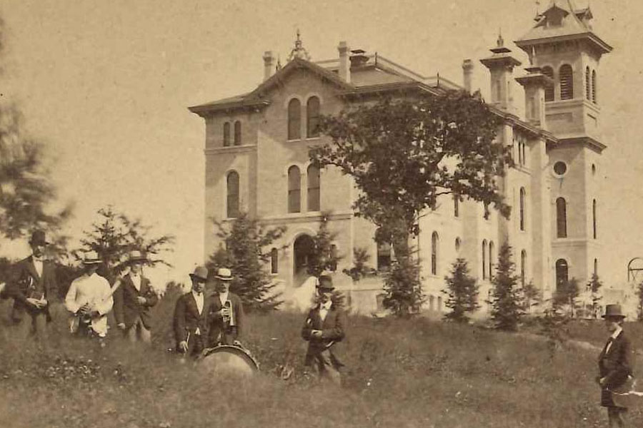 Old-time photo shows Old Main with people standing in front.