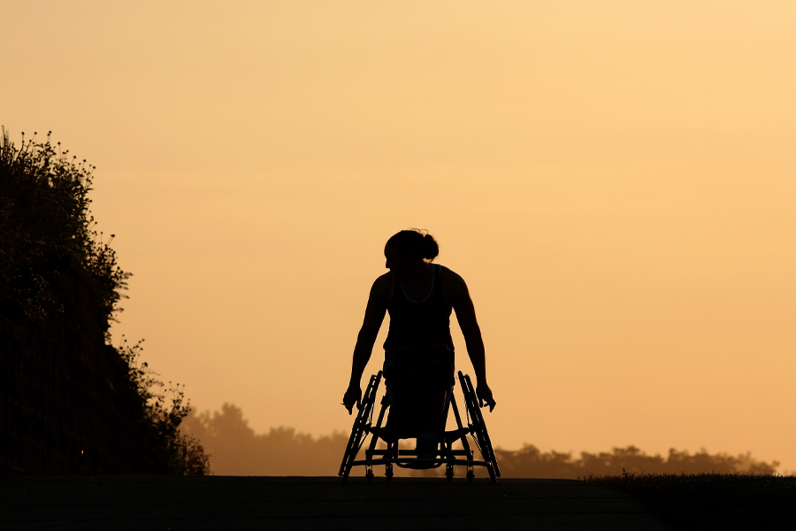 The silhouette of a person in a wheelchair against a sun setting sky.