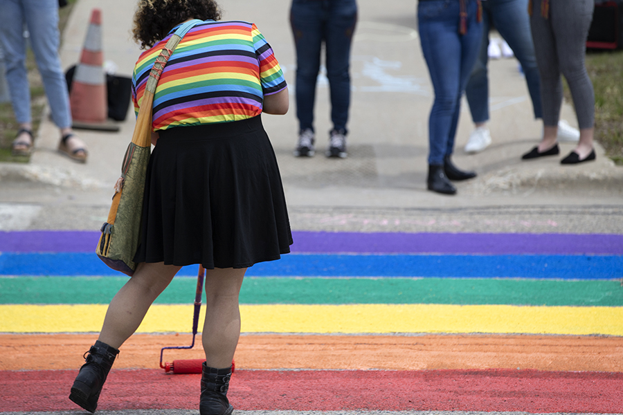 A person wearing a rainbow shirt helps to paint the road in rainbow shades.