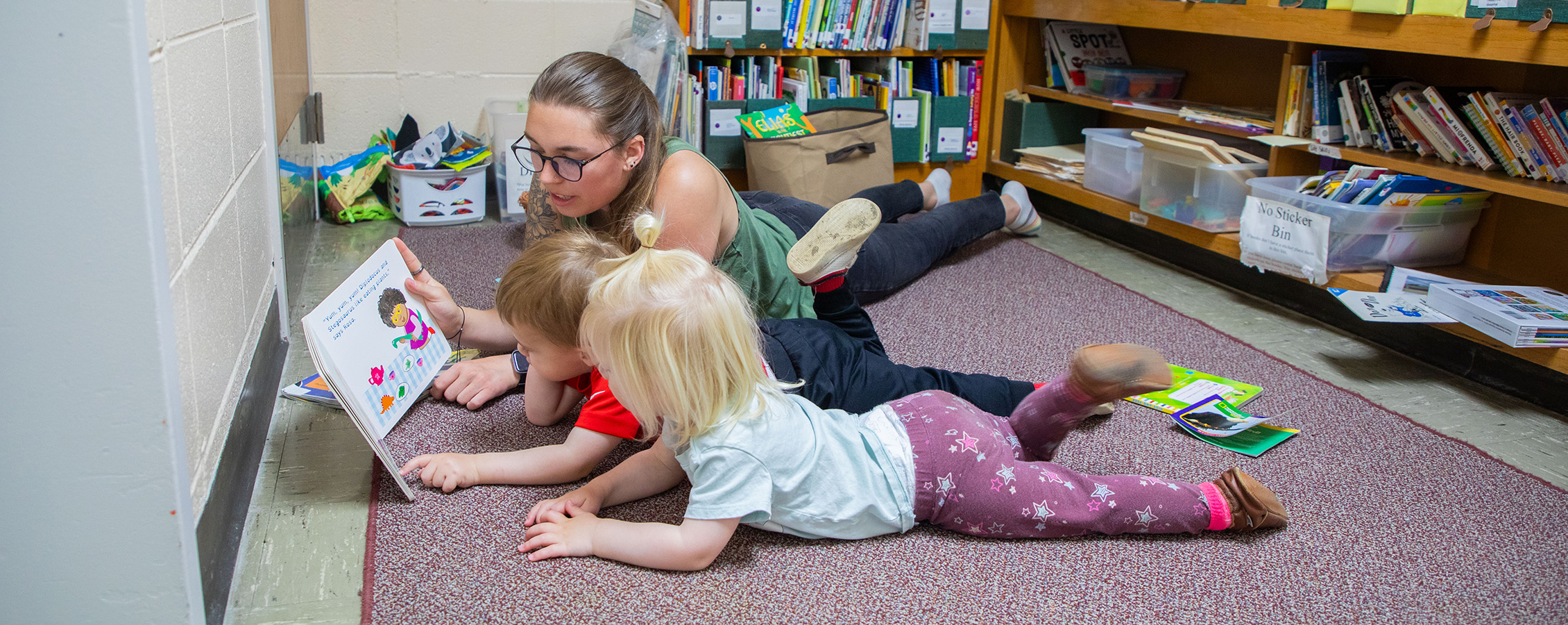A Children's Center teacher reads to a student while they both lie on the floor.
