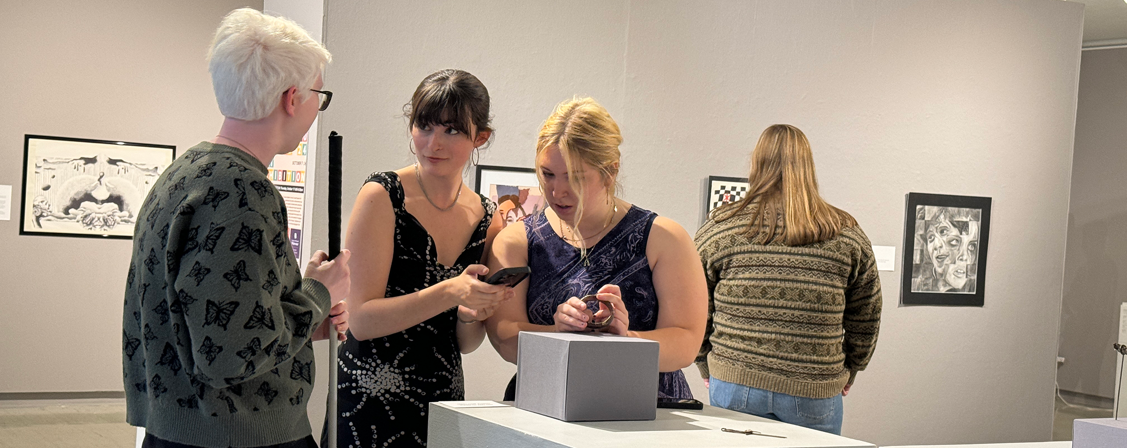 Three students interact as they look at a piece in the Crossman Gallery.