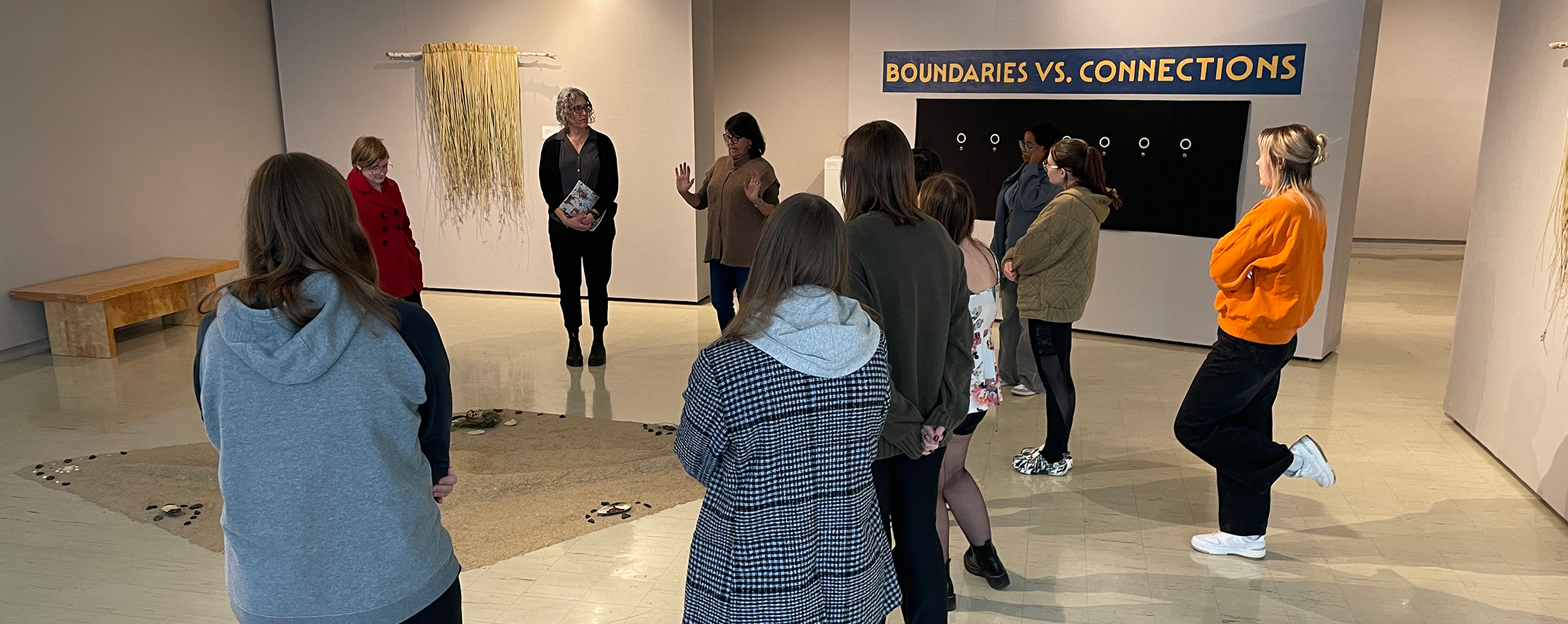 A group of people stand around an exhibit made with sand and a sign in the background that says Boundaries vs. Connections.